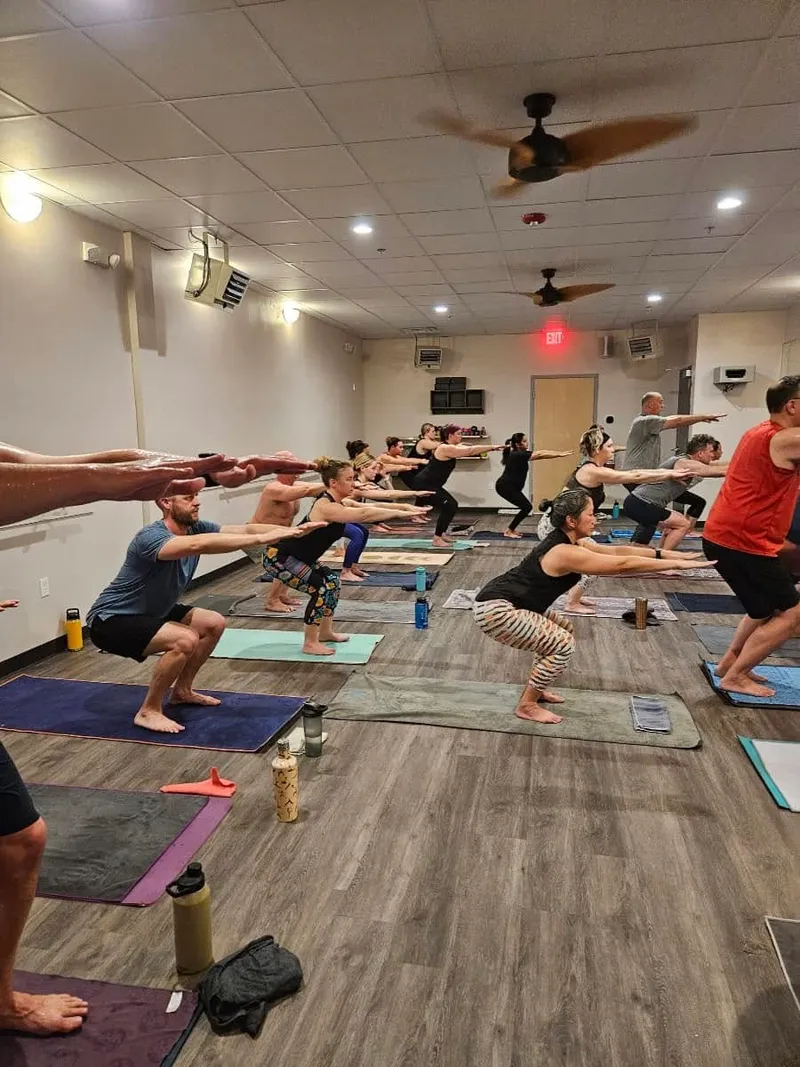 Chair pose with arms extended in a full hot yoga class